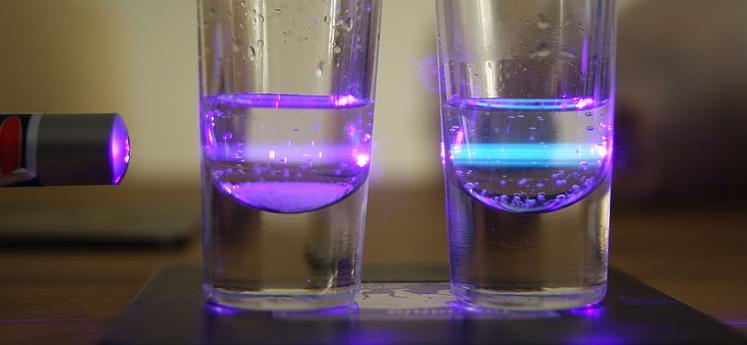 Duas amostras de quinino dissolvido em água com um laser violeta (à esquerda) iluminando ambas. Pode-se observar a fluorescência azul do quinino no copo da direita. A amostra da esquerda contém íons cloreto, que suprime a fluorescência do quinino, e por isso observa-se apenas a luz violeta refratada do laser.(Fonte: http://en.wikipedia.org/)